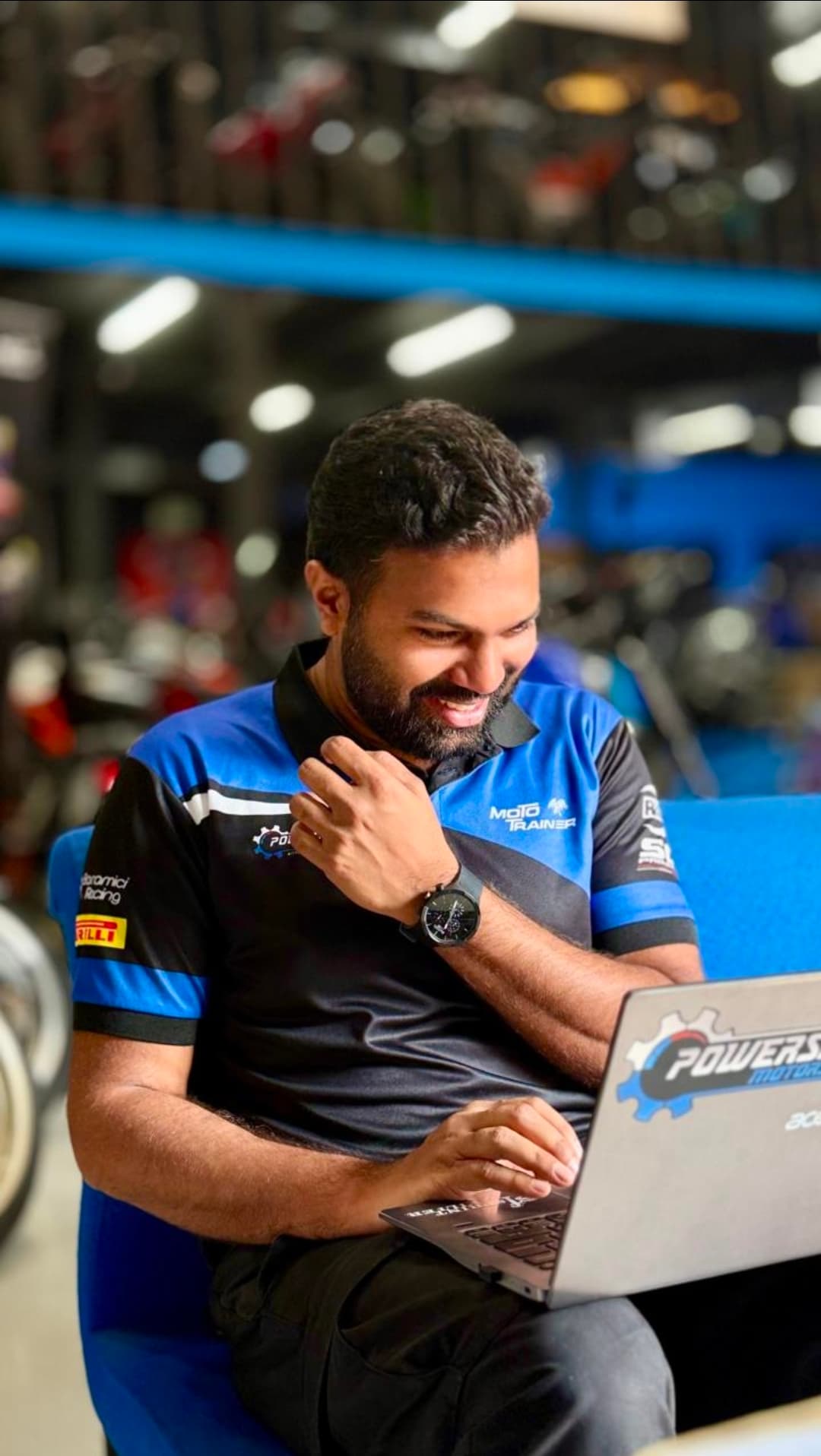Smiling man in a blue racing polo shirt works on a laptop in a showroom.