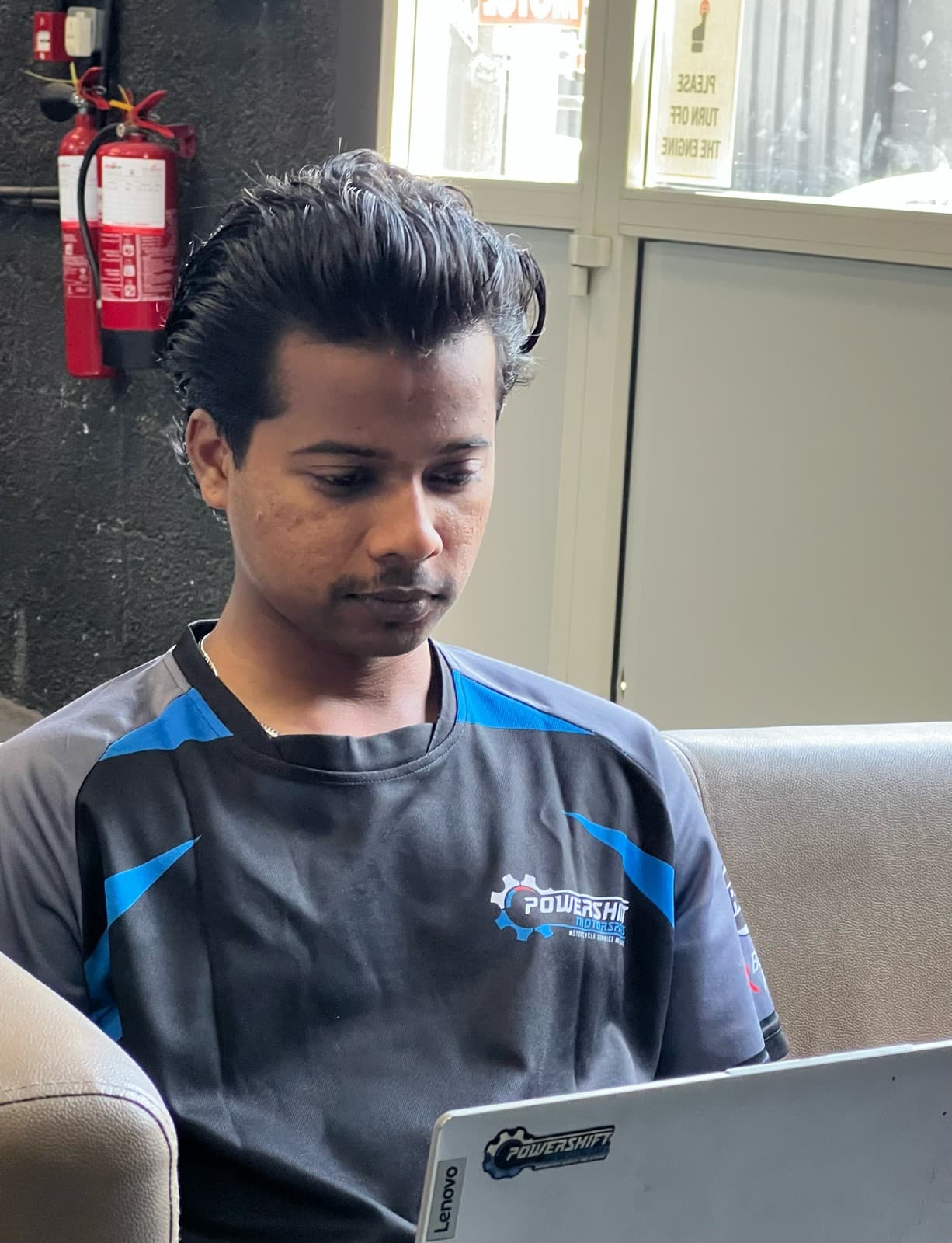 Man in a Powershift Motorsports shirt looks at a laptop while sitting on a couch.