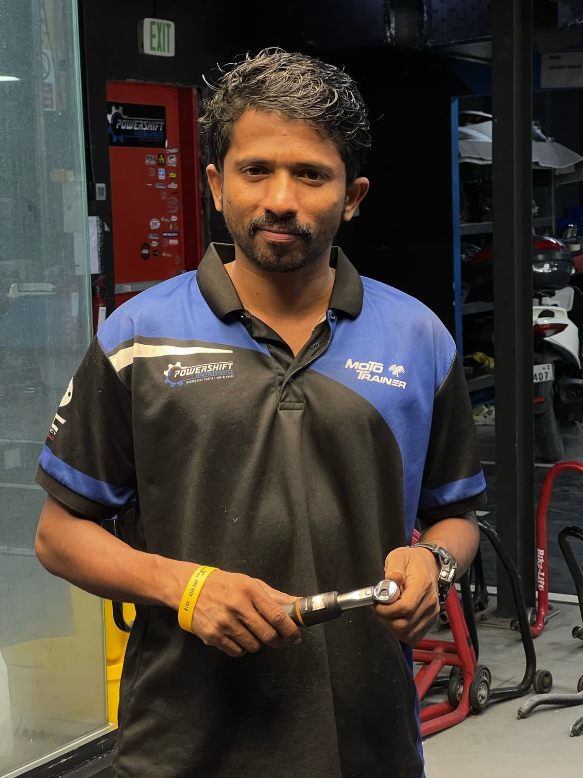 Mechanic in a blue and black polo shirt holding a torque wrench in a workshop.