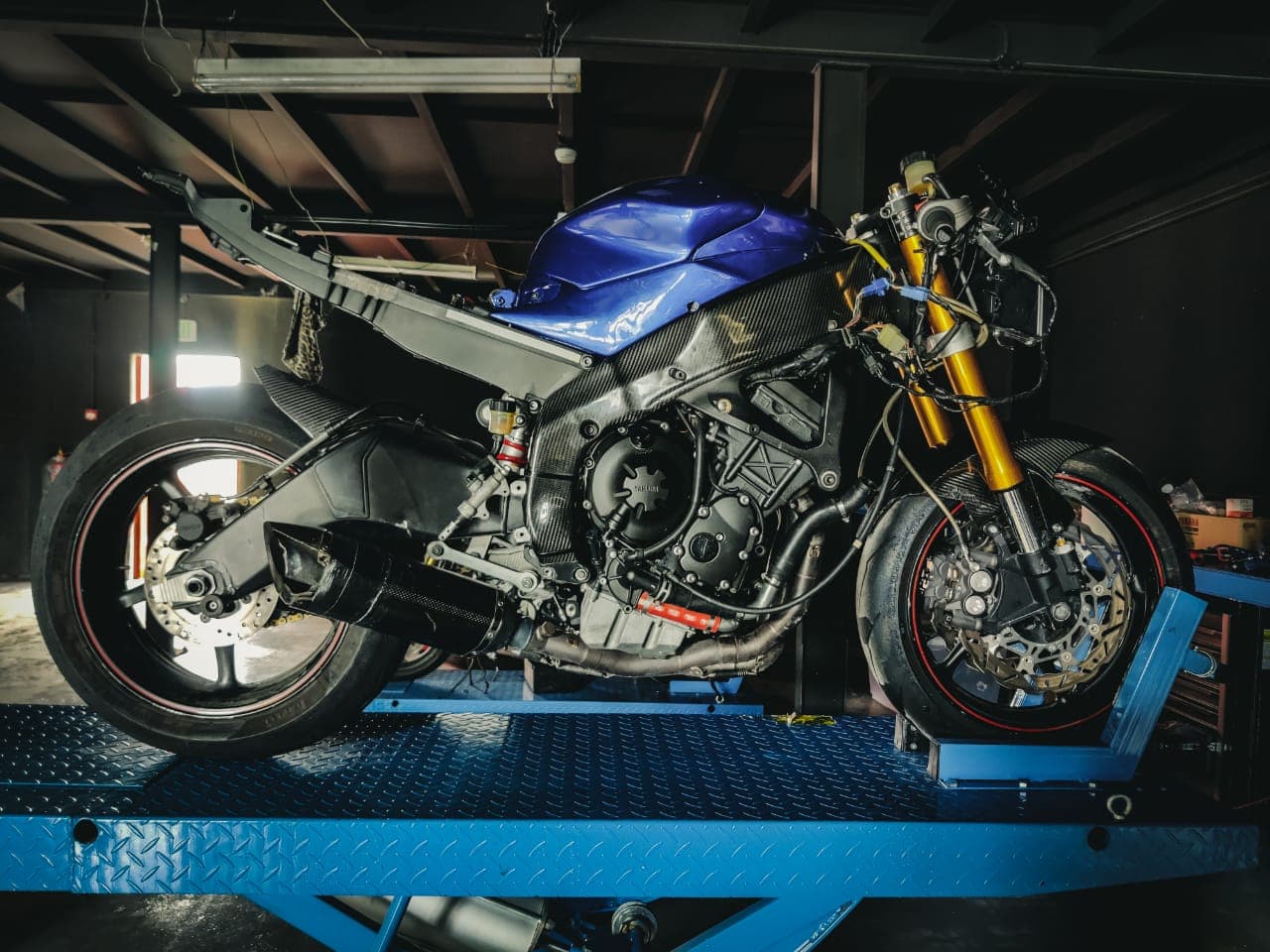 Partially disassembled blue sport motorcycle on a blue hydraulic lift inside a dark garage.